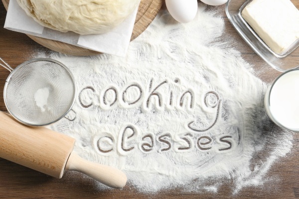 Text written on flour and ingredients, wooden background. Cooking classes concept